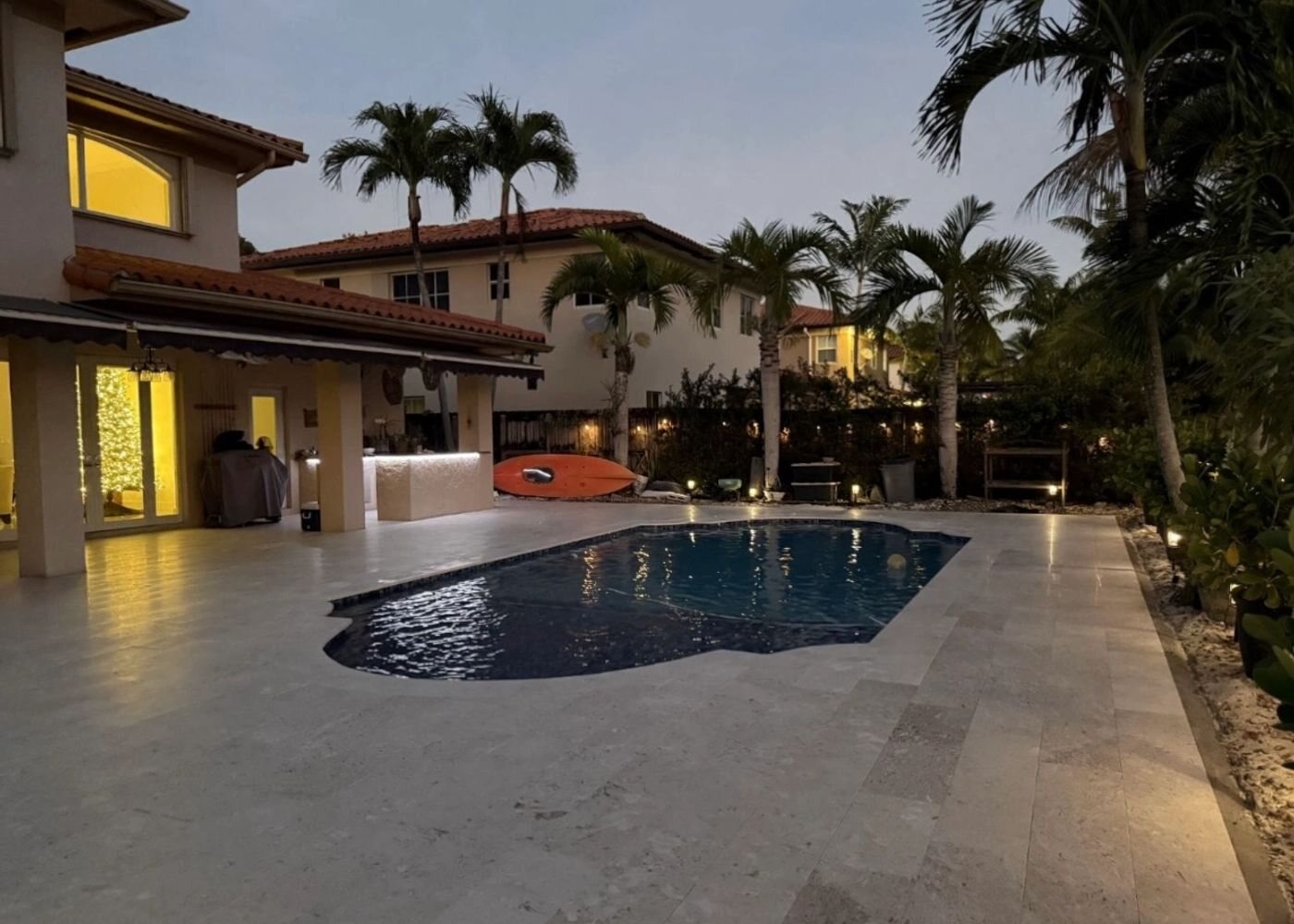 Travertine pool deck and lit Miami home at dusk, All Around Turf & Pavers